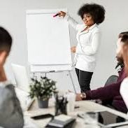 Présentation d'une femme devant un tableau avec des participants attentifs.